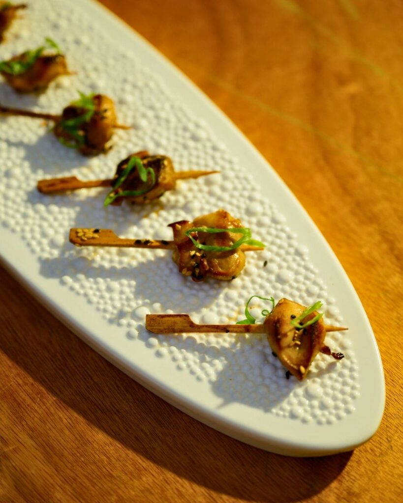 Elegant grilled skewers garnished with fresh herbs served on a textured white platter at a tropical wedding.