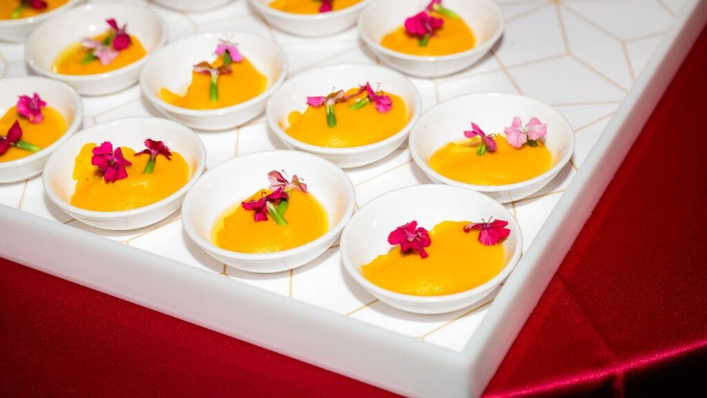 Small white bowls of vibrant golden puree topped with pink edible flowers