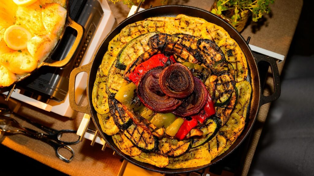 Grilled vegetables including zucchini, eggplant, bell peppers, and red onions arranged in a cast iron skillet.