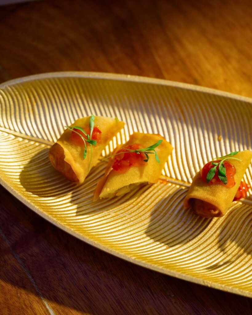 Golden crispy spring rolls garnished with fresh microgreens and chili sauce, beautifully plated for a wedding reception.