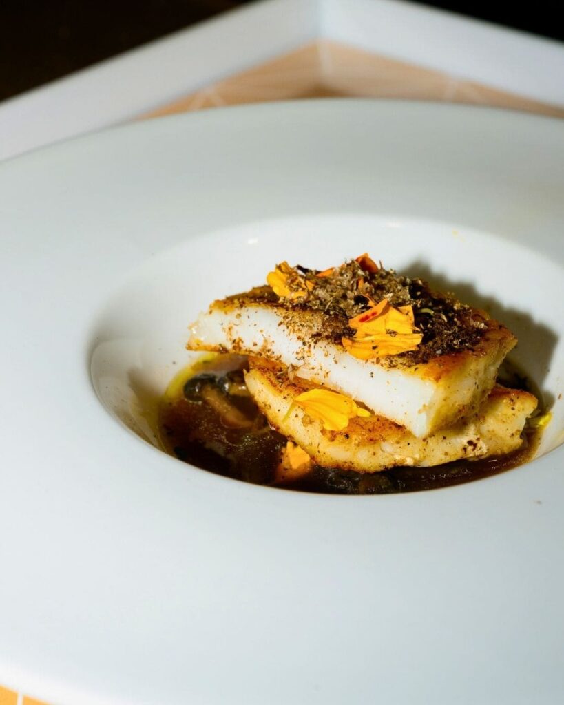 Plated white fish garnished with spice and edible flowers