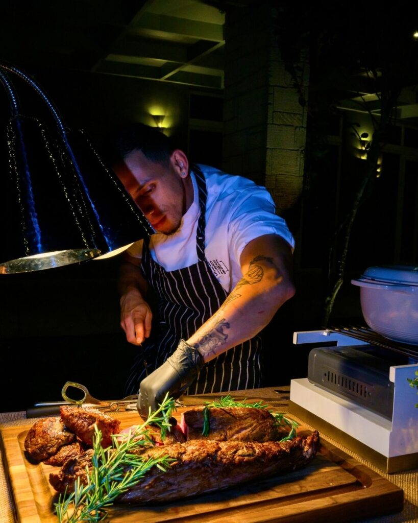 Chef carving prime rib roast at live carving station with fresh rosemary garnish