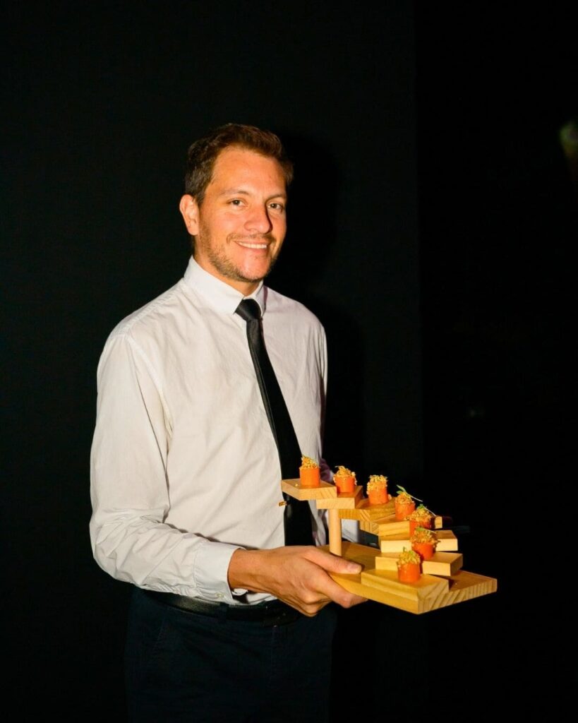 Server holding geometric wooden tray of colorful canapés