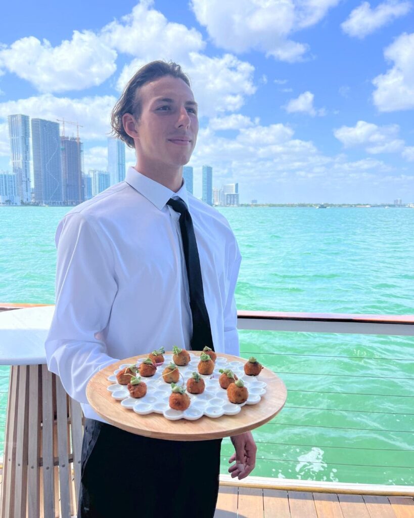 UCD server passing arancini with Miami skyline in background