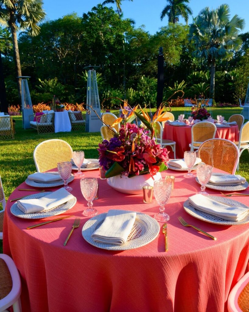 Elegant outdoor wedding table setup with coral linens, gold flatware, and a tropical floral centerpiece at Fairchild Tropical Botanic Garden.