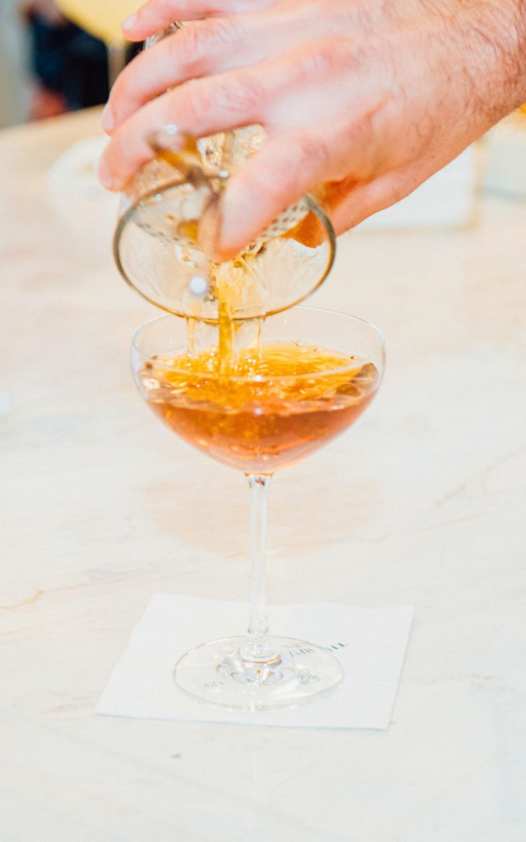 Bartender pouring a golden cocktail into a coupe glass.