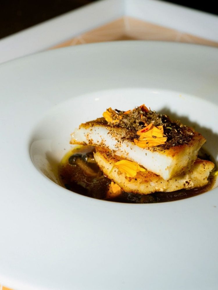 Plated white fish garnished with spice and edible flowers