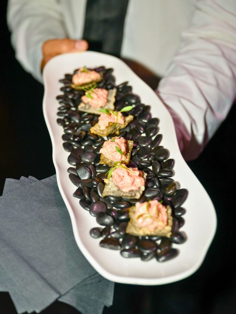 Elegant hors d’oeuvres displayed on a bed of black stones at a Miami event.