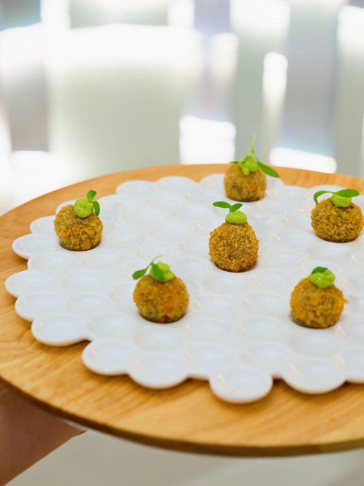 Crispy golden hors d’oeuvres topped with green garnish on a modern tray.