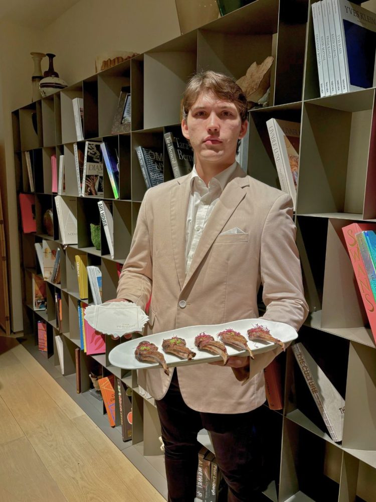 Server holding a tray of gourmet lamb chops at a luxury event.