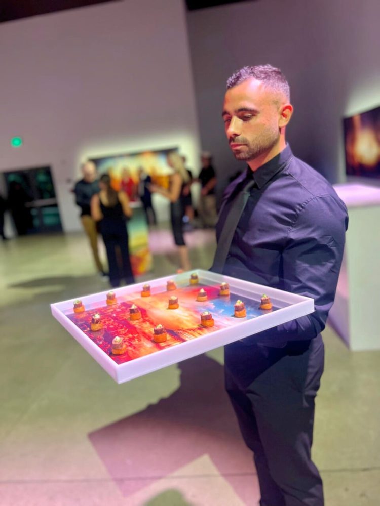 Server holding colorful art-inspired tray of hors d’oeuvres at gallery event