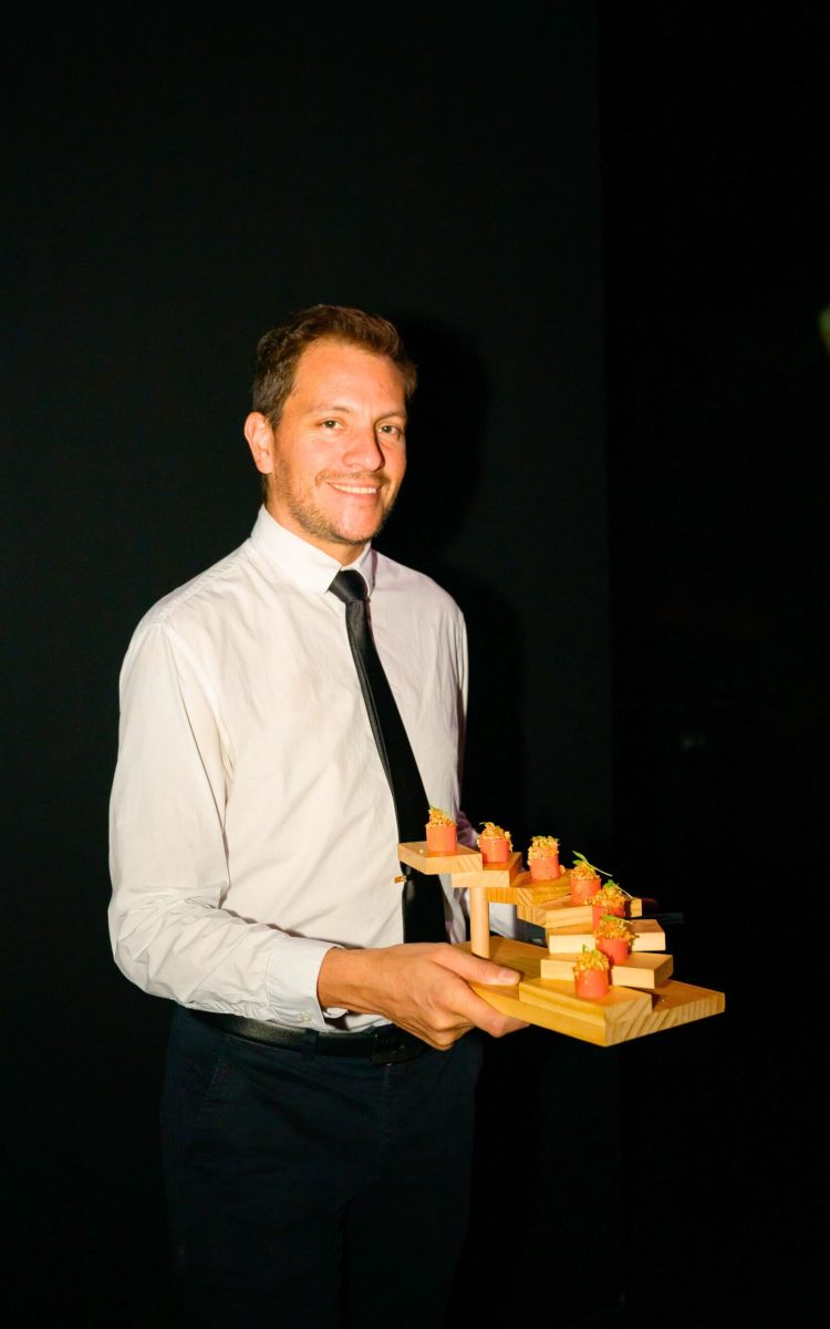 Formal server offering tiered wooden tray of gourmet canapés.
