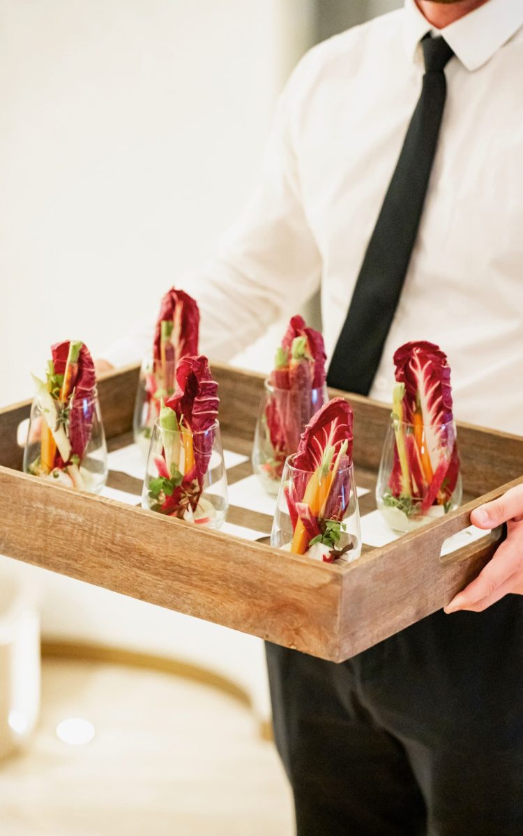 Server presenting individual glass crudités with vibrant radicchio and fresh vegetables.